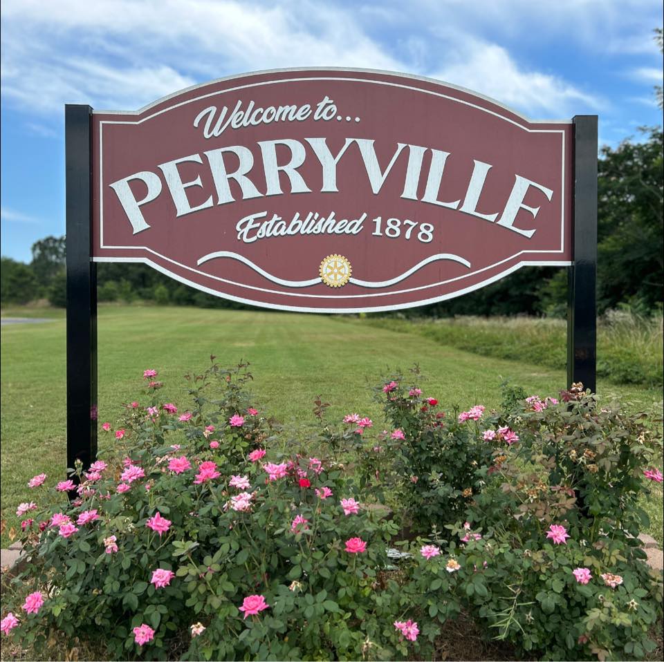 Photograph showing a sign that says "Welcome to Perryville, established 1878". Decorative flowers are in the foreground below the sign.
